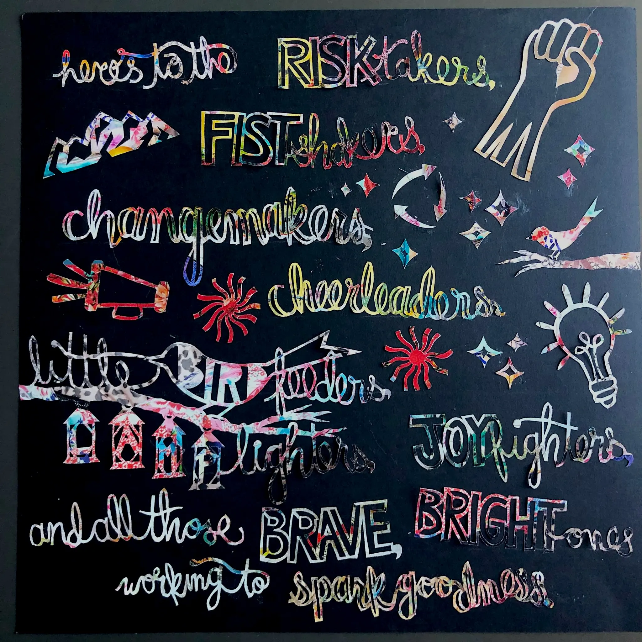 the quote 'Here's to the risktakers, fistshakers, changemakers, cheerleaders, little bird feeders, lamp lighters, joy fighters, and all the brave, bright ones working to spark goodness' cut out of Johnny Was catalogue paper on a black background