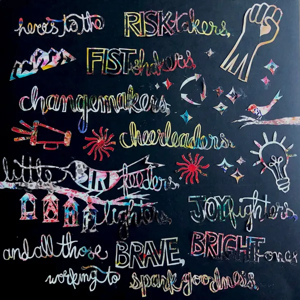 the quote 'Here's to the risktakers, fistshakers, changemakers, cheerleaders, little bird feeders, lamp lighters, joy fighters, and all the brave, bright ones working to spark goodness' cut out of Johnny Was catalogue paper on a black background