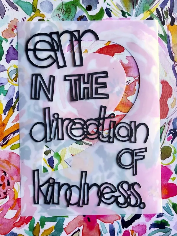 floral wrapping paper background with translucent vellum over; the words "Err in the direction of kindness." cut out of black paper on top.