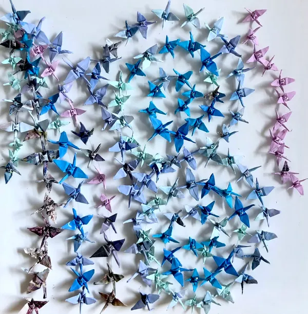 small paper cranes in shades of blue and purple in lines following the shape of a B, pinned to a white background